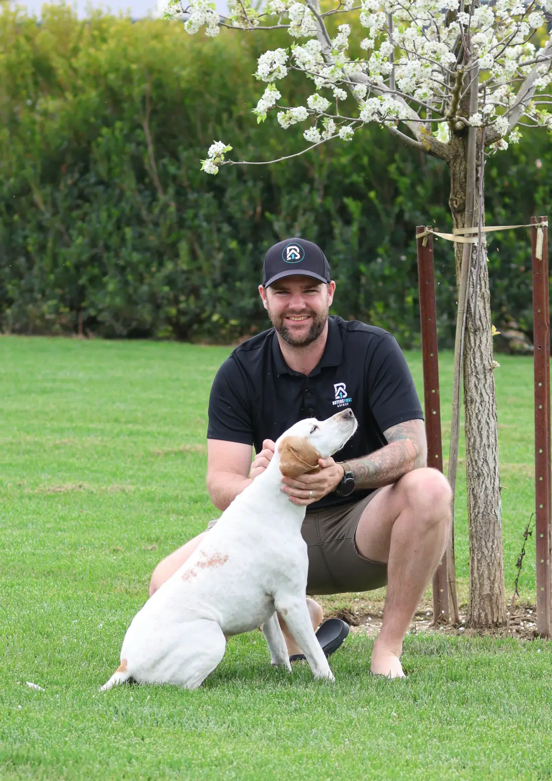 Dan White crouched on the lawn with his dog under a blossoming tree